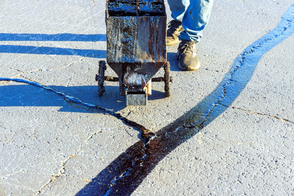 A worker applying the crack sealant to a damaged asphalt driveway to prevent further deterioration.